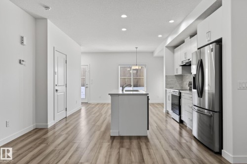 Open concept living area featuring wood-finish flooring, recessed lighting, a kitchen island with sink, stainless steel appliances, and white cabinetry - 4853 Alwood Point(E) Sw, Edmonton, AB - Indoor Photo Showing Kitchen