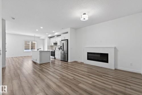 Open-concept living area with wood-finish flooring, a contemporary electric fireplace, and recessed lighting - 4853 Alwood Point(E) Sw, Edmonton, AB - Indoor With Fireplace