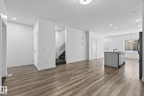 Open-concept living area featuring wood-finish flooring, recessed lighting, and a kitchen island with an undermount sink - 4853 Alwood Point(E) Sw, Edmonton, AB - Indoor Photo Showing Kitchen