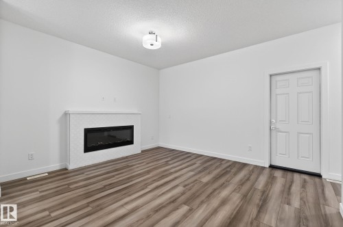 Wood-finish flooring, white walls, built-in fireplace with geometric tile surround, flush mount ceiling light, and a paneled entry door - 4853 Alwood Point(E) Sw, Edmonton, AB - Indoor Photo Showing Living Room With Fireplace