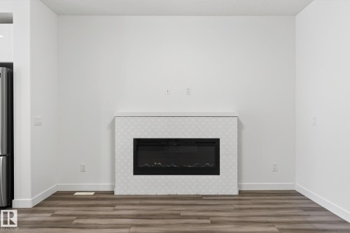 Electric fireplace with a tiled surround and mantle, set against white walls and wood-finish flooring - 4853 Alwood Point(E) Sw, Edmonton, AB - Indoor Photo Showing Living Room With Fireplace