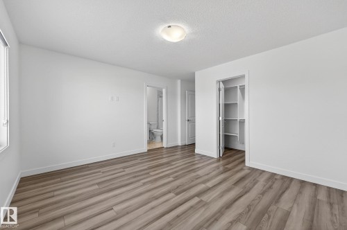 Wood-finish flooring, white walls, flush mount lighting, built-in closet shelving, and a window with roller shade - 4853 Alwood Point(E) Sw, Edmonton, AB - Indoor Photo Showing Other Room