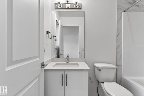 White vanity with integrated sink and chrome faucet, rectangular mirror, brushed nickel light fixture, white toilet, and tub with large format tile surround - 4853 Alwood Point(E) Sw, Edmonton, AB - Indoor Photo Showing Bathroom