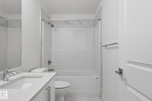 White vanity with an integrated sink and chrome faucet, white bathtub with a shower, and marble-look wall tile - 4853 Alwood Point(E) Sw, Edmonton, AB - Indoor Photo Showing Bathroom