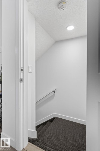 Staircase featuring dark patterned carpeting, a metal handrail, recessed lighting, and white trim - 4853 Alwood Point(E) Sw, Edmonton, AB - Indoor Photo Showing Other Room