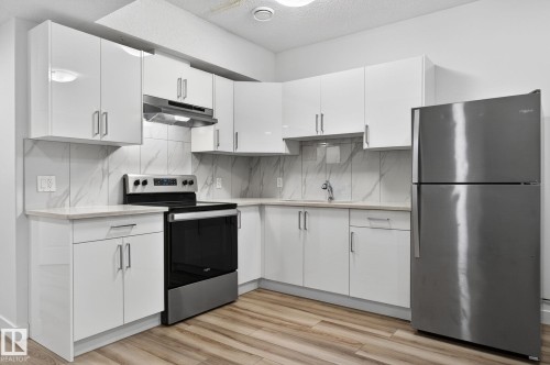 L-shaped kitchen with white cabinetry, stainless steel appliances, stone-finish countertops, tile backsplash, and wood-finish flooring - 4853 Alwood Point(E) Sw, Edmonton, AB - Indoor Photo Showing Kitchen With Upgraded Kitchen
