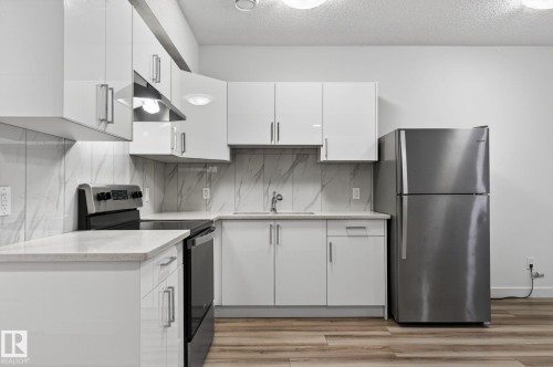 Kitchen featuring white cabinetry, light-toned countertops, a stainless steel refrigerator, a black range, and wood-finish flooring - 4853 Alwood Point(E) Sw, Edmonton, AB - Indoor Photo Showing Kitchen