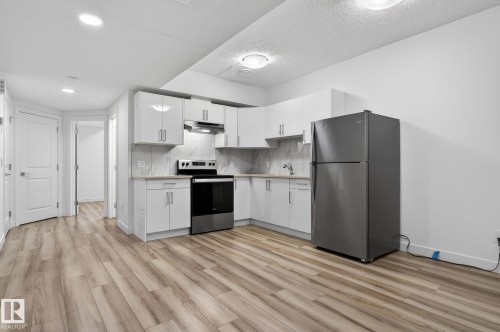 Contemporary kitchen featuring white cabinetry, stainless steel appliances, light-toned countertops, and a full-height backsplash - 4853 Alwood Point(E) Sw, Edmonton, AB - Indoor Photo Showing Kitchen