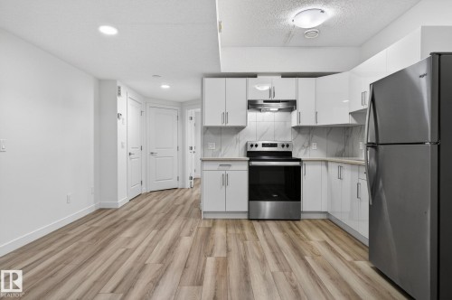 Kitchen featuring white cabinetry, stainless steel appliances, marble-look backsplash, light-toned countertops, and wood-finish flooring - 4853 Alwood Point(E) Sw, Edmonton, AB - Indoor Photo Showing Kitchen
