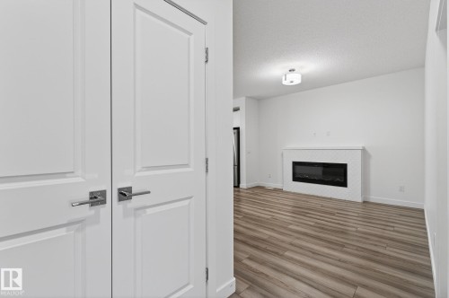 Wood-finish flooring, white walls, and an electric fireplace with a white tiled surround and mantel - 4853 Alwood Point(E) Sw, Edmonton, AB - Indoor Photo Showing Other Room With Fireplace