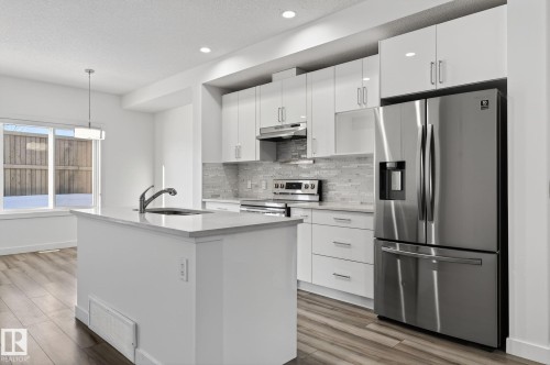 Modern kitchen featuring white cabinetry, a stainless steel refrigerator, and a kitchen island with an integrated sink - 4853 Alwood Point(E) Sw, Edmonton, AB - Indoor Photo Showing Kitchen With Upgraded Kitchen