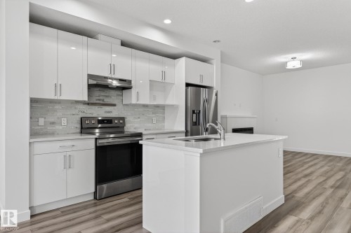 Modern kitchen featuring white cabinetry, stainless steel appliances, a center island with a sink, and wood-finish flooring - 4853 Alwood Point(E) Sw, Edmonton, AB - Indoor Photo Showing Kitchen With Upgraded Kitchen