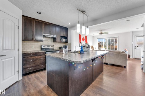 Kitchen featuring dark wood-finish cabinetry, light tile backsplash, and a central island with an integrated sink - 2040 24 Street Nw, Edmonton, AB - Indoor Photo Showing Kitchen With Upgraded Kitchen