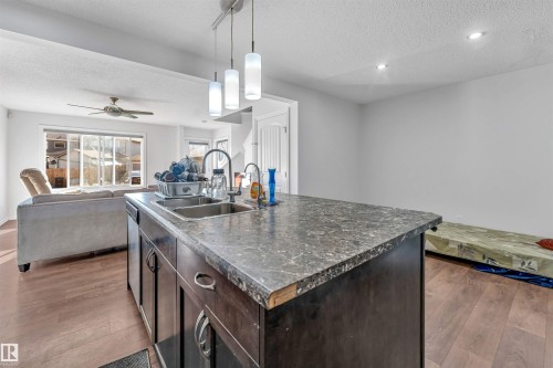 Kitchen island with double basin stainless steel sink, dark cabinetry, and pendant lighting - 2040 24 Street Nw, Edmonton, AB - Indoor Photo Showing Kitchen With Double Sink