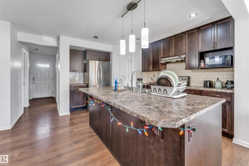 Kitchen featuring wood-finish flooring, dark wood cabinetry, a center island with a stone-finish countertop, and stainless steel appliances - 2040 24 Street Nw, Edmonton, AB - Indoor Photo Showing Kitchen With Upgraded Kitchen
