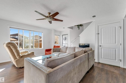 Wood-finish flooring, white walls, large multi-pane window, ceiling fan with integrated lighting, and a white panel door - 2040 24 Street Nw, Edmonton, AB - Indoor Photo Showing Living Room