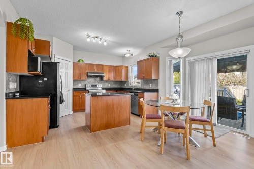 Kitchen featuring wood-finish cabinetry, dark countertops, a tiled backsplash, and a central island - 3403 23 Nw, Edmonton, AB - Indoor Photo Showing Kitchen