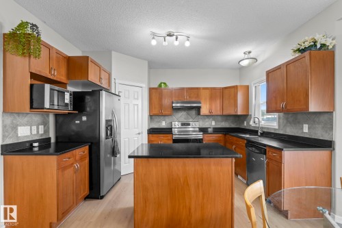 Kitchen featuring wood cabinetry, dark countertops, a central island, and stainless steel appliances - 3403 23 Nw, Edmonton, AB - Indoor Photo Showing Kitchen