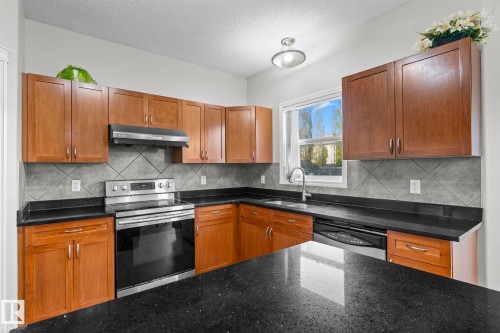 Kitchen featuring wood cabinetry, black countertops, stainless steel appliances, and a tile backsplash - 3403 23 Nw, Edmonton, AB - Indoor Photo Showing Kitchen