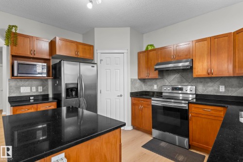 Kitchen featuring wood cabinetry, stainless steel appliances, dark countertops, and tiled backsplash - 3403 23 Nw, Edmonton, AB - Indoor Photo Showing Kitchen