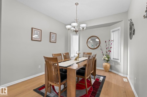 Recessed bay window with vertical blinds, wood-finish flooring, and a chandelier with frosted glass shades - 3403 23 Nw, Edmonton, AB - Indoor Photo Showing Dining Room