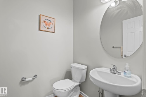 Pedestal sink with chrome faucet, circular wall mirror, and overhead vanity lighting - 3403 23 Nw, Edmonton, AB - Indoor Photo Showing Bathroom