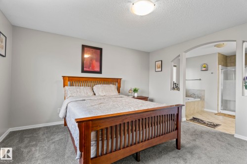 Carpeted bedroom with overhead lighting and an arched doorway leading to a bathroom featuring a built-in tub and a glass-enclosed shower - 3403 23 Nw, Edmonton, AB - Indoor Photo Showing Bedroom