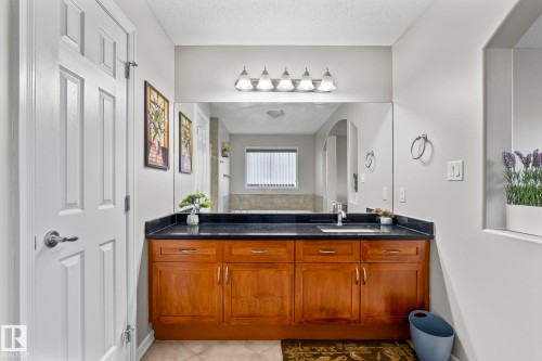 Vanity with wood-finish cabinetry and a dark countertop, undermount sink, and polished chrome faucet - 3403 23 Nw, Edmonton, AB - Indoor
