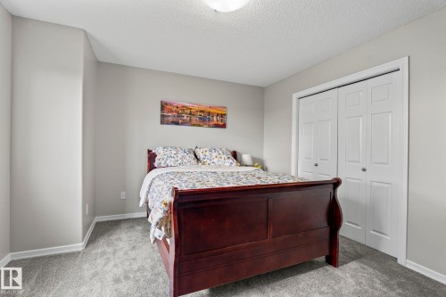 Soft gray wall paint, textured ceiling, gray carpet flooring, and bi-fold closet doors - 3403 23 Nw, Edmonton, AB - Indoor Photo Showing Bedroom