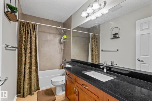 Hardwood-finish flooring, a wood vanity with a dark countertop, an integrated sink, a large wall-mounted mirror, and a tub with tile surround - 3403 23 Nw, Edmonton, AB - Indoor Photo Showing Bathroom