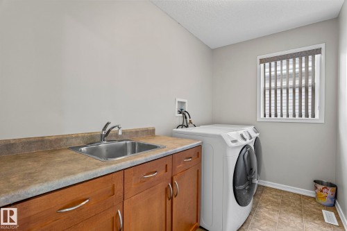 Dedicated laundry area featuring a stainless steel sink, wood-finish cabinetry, and neutral flooring - 3403 23 Nw, Edmonton, AB - Indoor Photo Showing Laundry Room