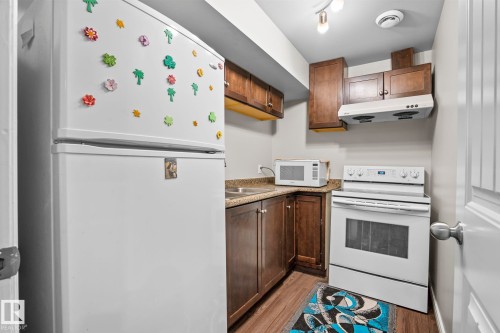 Compact kitchen featuring wood-finish cabinetry, a white electric range, and a white refrigerator - 3403 23 Nw, Edmonton, AB - Indoor Photo Showing Kitchen