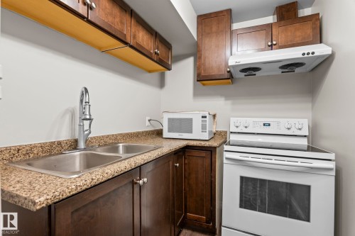 Kitchenette featuring a stainless steel double-basin sink, chrome pull-down faucet, brown wood-finish cabinetry, and light speckled countertops - 3403 23 Nw, Edmonton, AB - Indoor Photo Showing Kitchen With Double Sink