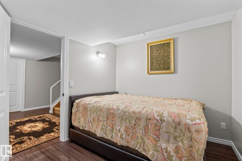 Wood-finish flooring throughout, white trim, and a wall-mounted light fixture - 3403 23 Nw, Edmonton, AB - Indoor Photo Showing Bedroom
