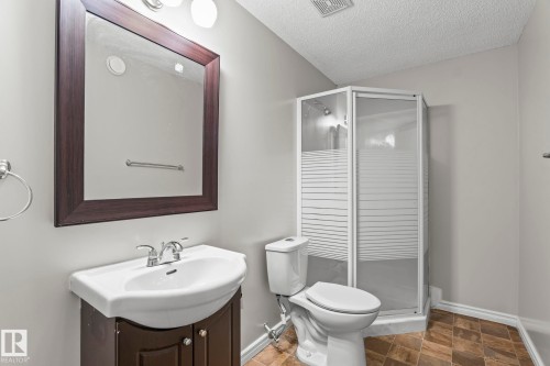 Corner shower enclosure with frosted glass, vanity with integral sink, wood-finish cabinet, and framed mirror - 3403 23 Nw, Edmonton, AB - Indoor Photo Showing Bathroom