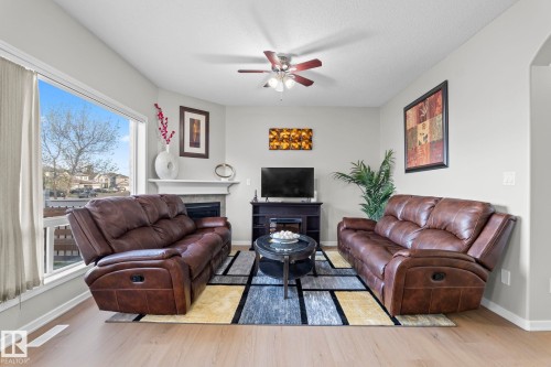 Hardwood-finish flooring, corner fireplace with mantel, ceiling fan with light fixture, large picture window, and light-toned walls - 3403 23 Nw, Edmonton, AB - Indoor Photo Showing Living Room With Fireplace
