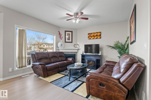 Living area with light-toned wood-finish flooring, a corner fireplace with mantel, and a ceiling fan with integrated lighting - 3403 23 Nw, Edmonton, AB - Indoor Photo Showing Living Room With Fireplace