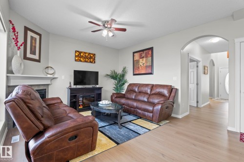 Living area with fireplace, wood-finish flooring, ceiling fan, and arched entryway - 3403 23 Nw, Edmonton, AB - Indoor Photo Showing Living Room With Fireplace