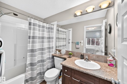 Bathroom featuring a bathtub with an integrated shower, a vanity with a drop-in sink, a speckled countertop, a tiled backsplash, and a large wall mirror with overhead lighting - 466 Chappelle Drive Sw, Edmonton, AB - Indoor Photo Showing Bathroom