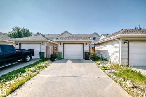 Concrete driveway with a single-car garage featuring a white overhead door and exterior wall sconce lighting - 466 Chappelle Drive Sw, Edmonton, AB - Outdoor With Facade