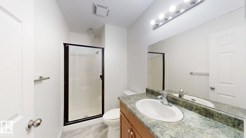 Full-size mirror with vanity lighting, a single vanity with an integrated sink, a dark green countertop, and a glass-enclosed shower with a dark frame - 2426 33A Street Nw, Edmonton, AB - Indoor Photo Showing Bathroom