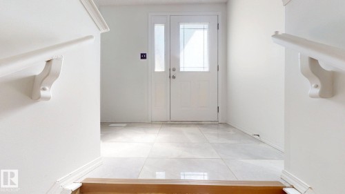 Entryway featuring a white paneled door with decorative glass inserts, ceramic tile flooring, and a white handrail with decorative brackets - 2426 33A Street Nw, Edmonton, AB - Indoor Photo Showing Other Room