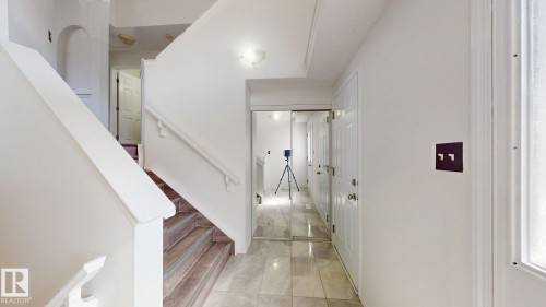 Tiled flooring at entry with wood-finish stairs and a white railing - 2426 33A Street Nw, Edmonton, AB - Indoor Photo Showing Other Room