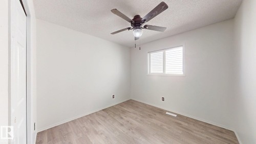 Recessed window with horizontal blinds, wood-finish flooring, ceiling fan with integrated lighting, and a white paneled door - 2426 33A Street Nw, Edmonton, AB - Indoor Photo Showing Other Room