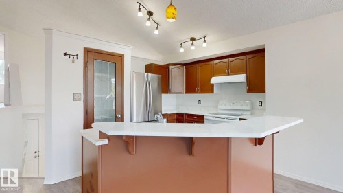 Kitchen featuring wood-finish cabinetry, white countertops, stainless steel refrigerator, and track lighting - 2426 33A Street Nw, Edmonton, AB - Indoor Photo Showing Kitchen