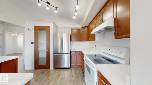 Kitchen featuring wood-finish flooring, white countertops, wood cabinetry, and stainless steel refrigerator - 2426 33A Street Nw, Edmonton, AB - Indoor Photo Showing Kitchen