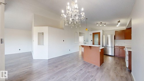 Vaulted ceilings with a prominent chandelier, wood-finish flooring, kitchen island with countertop, stainless steel refrigerator, and brown cabinetry - 2426 33A Street Nw, Edmonton, AB - Indoor Photo Showing Kitchen