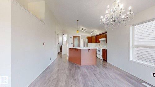 Spacious common area featuring wood-finish flooring, a decorative chandelier, and a kitchen with an island, rich wood-finish cabinetry, and white appliances - 2426 33A Street Nw, Edmonton, AB - Indoor Photo Showing Kitchen