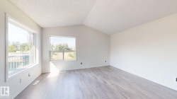 Vaulted ceiling, two windows, light-toned walls, wood-finish flooring, and white trim - 