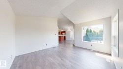 Light wood-finish flooring, vaulted ceiling, white interior walls, and a large window with white trim - 